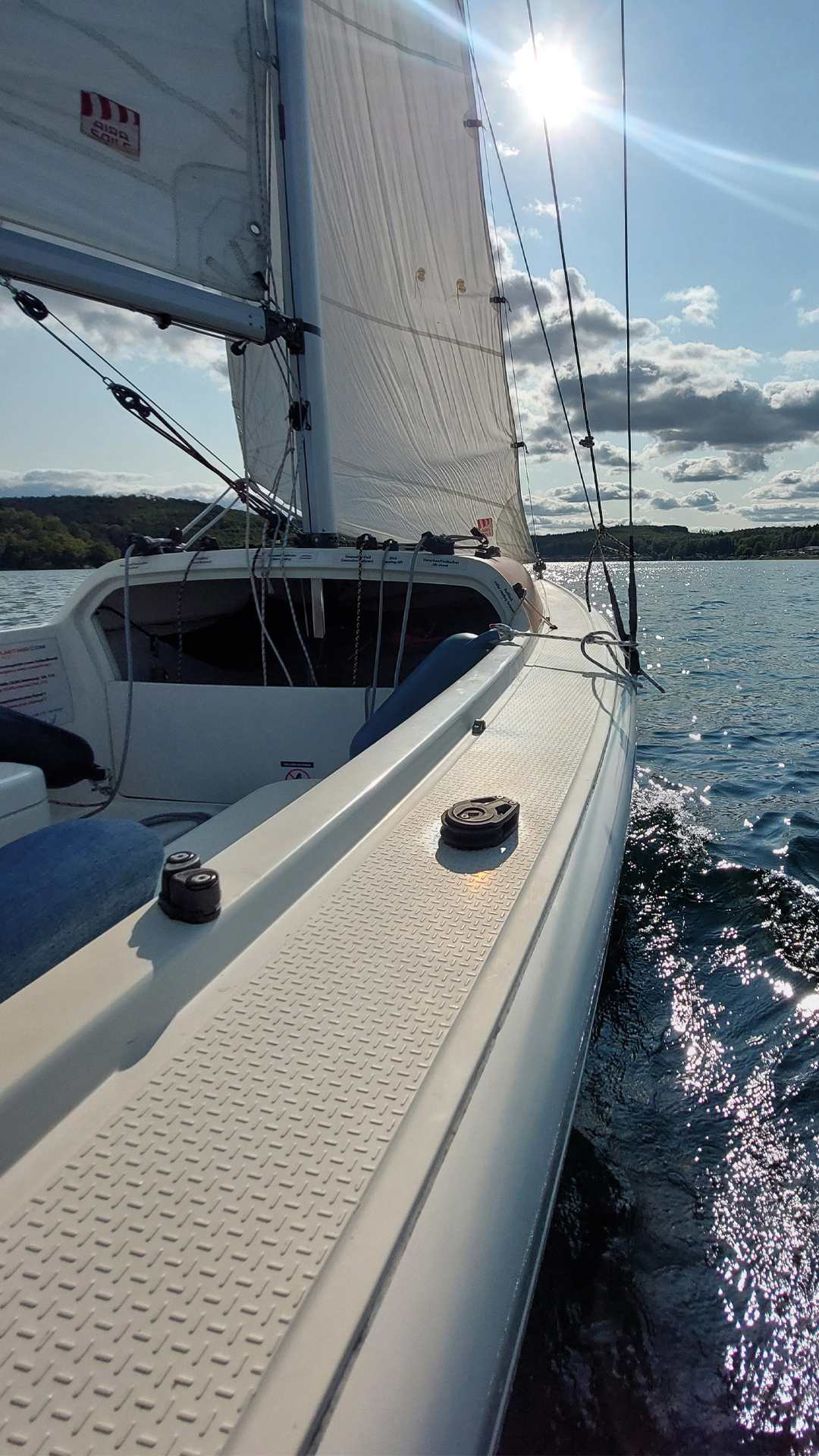 Sicht auf das Deck eines Sportsegelboots, welches über einen See fährt